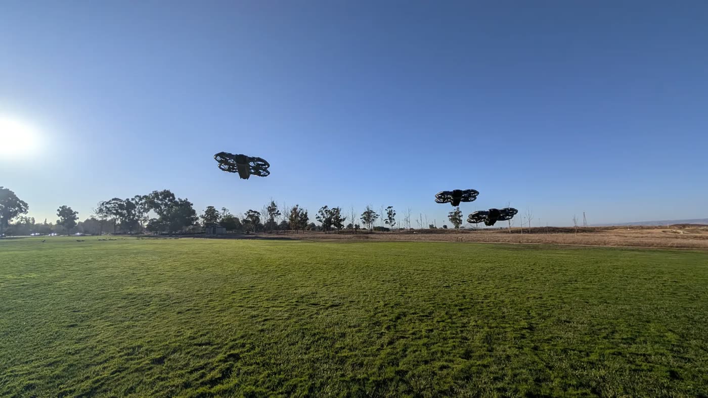 Three small drones hovering over a grass field against a blue sky