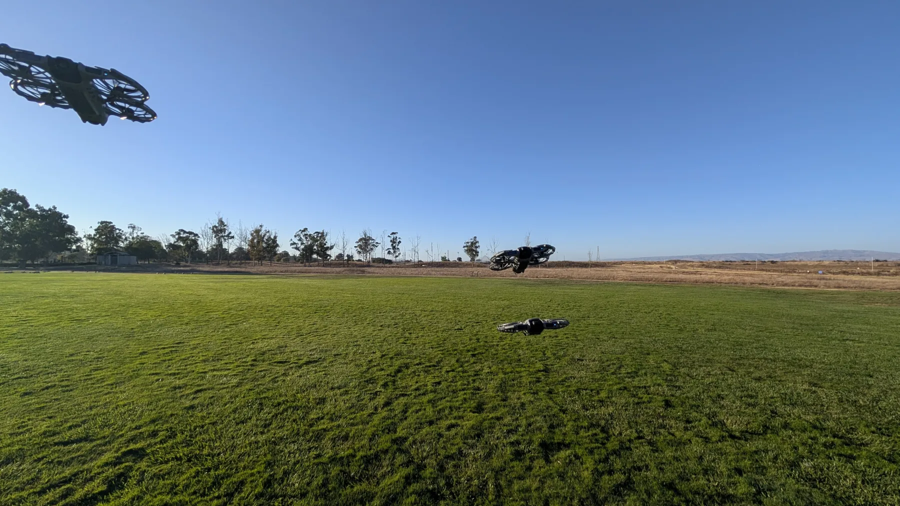Three Neo 2 drones hovering low over the grass